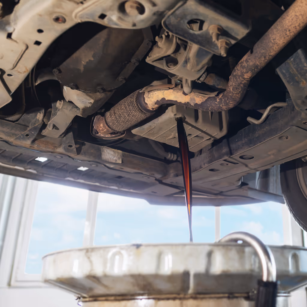 Dark, used engine oil draining from a car's oil pan into a large collection container during a professional mobile oil change by Maxamy Mobile Autocare.