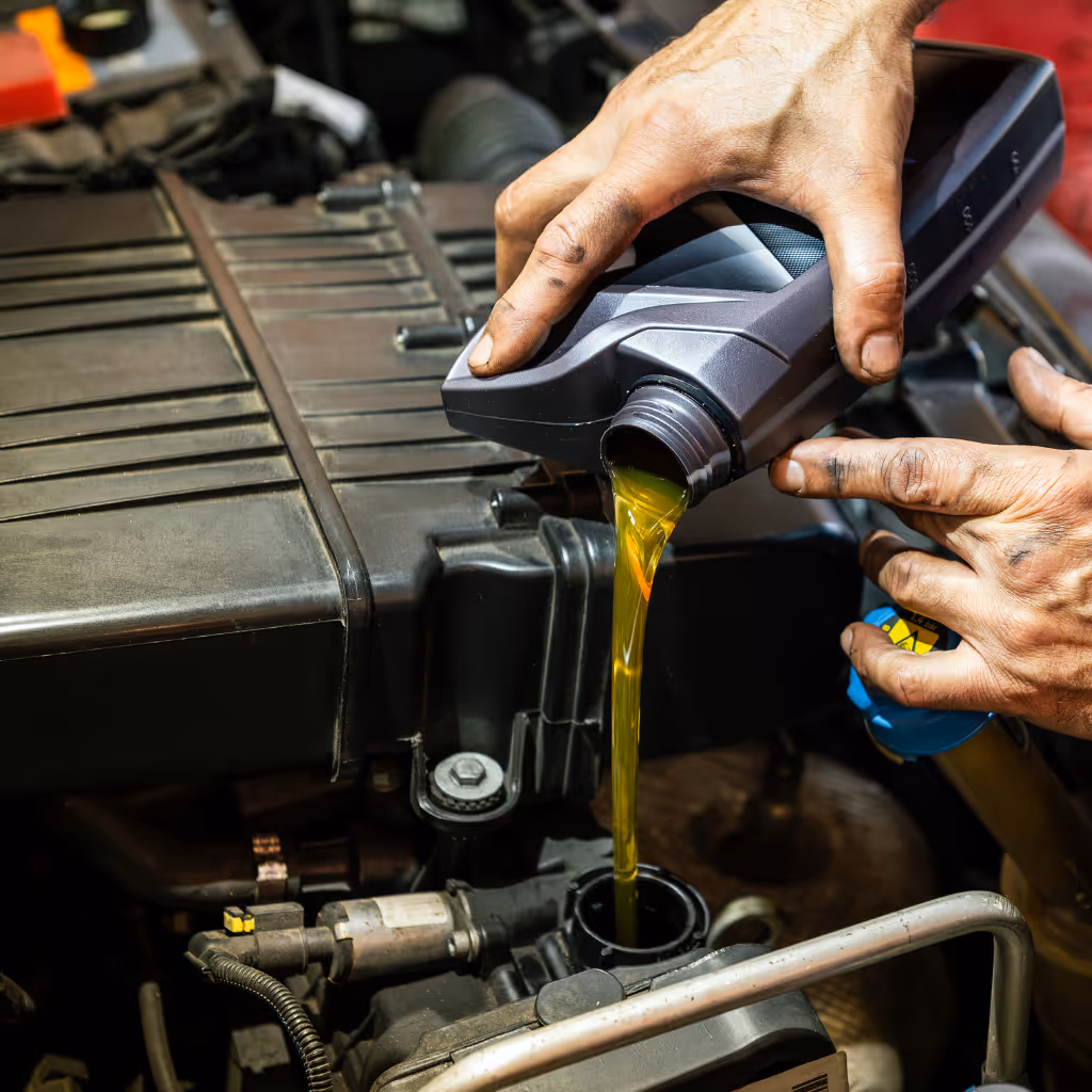 A mechanic's hands, dirty from work, pour fresh, golden engine oil from a bottle directly into a car's engine during a Maxamy Mobile Autocare service.