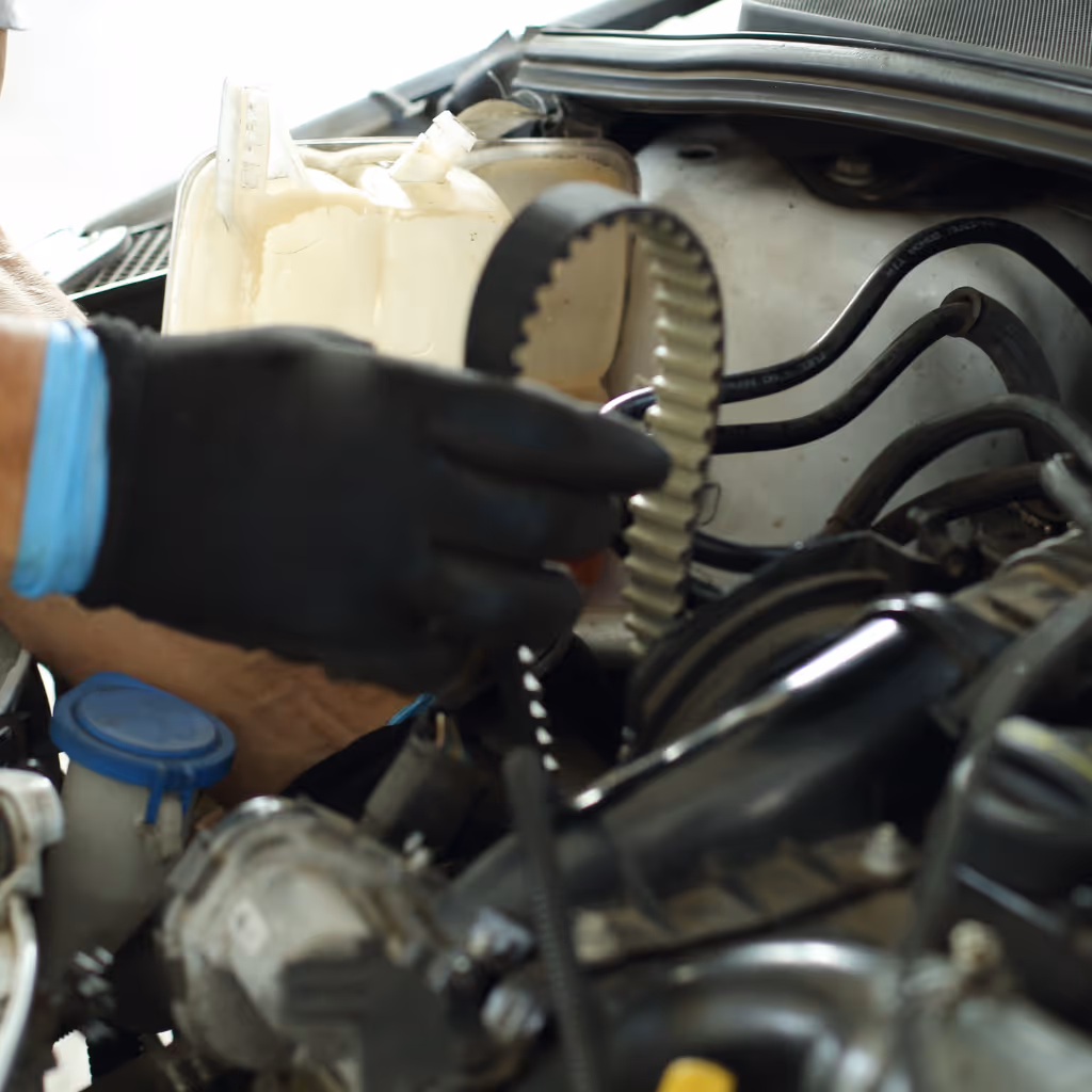 A Maxamy Mobile Autocare technician with gloved hands carefully installs a new timing belt into the engine bay of a customer's vehicle.