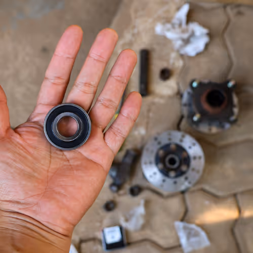 Hand holding a wheel bearing with car parts in the background, representing wheel bearing replacement and repair services in Slough, Maidenhead and Windsor.