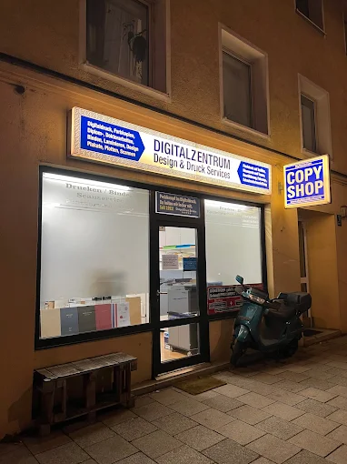 Night view of a Digitalzentrum copy shop storefront with illuminated signs and a scooter parked outside.
