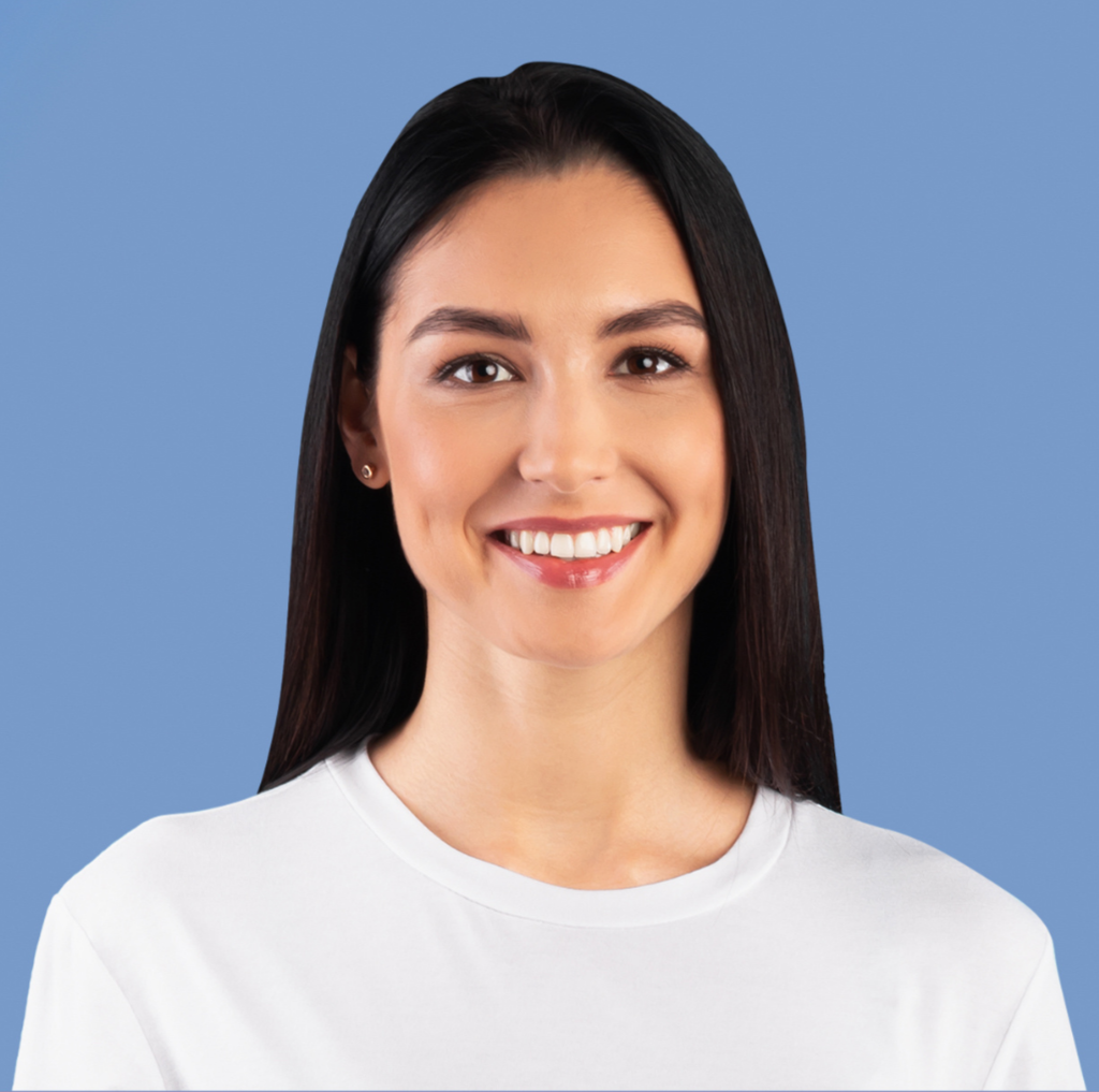 Smiling woman with long dark hair wearing a white shirt against a blue background.