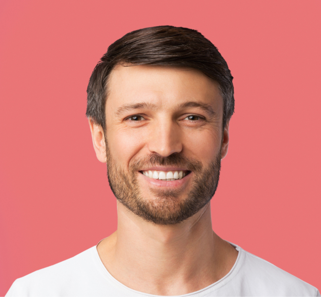 Smiling man with short dark hair and beard wearing a white shirt against a pink background.