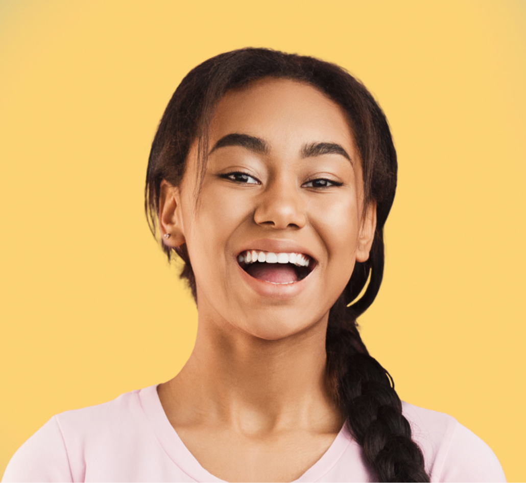Smiling young woman with braided hair wearing a light pink shirt against a yellow background.