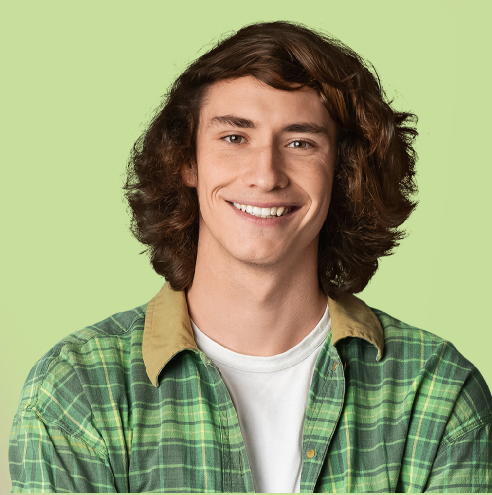 Young man with curly brown hair smiling, wearing a green plaid shirt over a white t-shirt against a light green background.