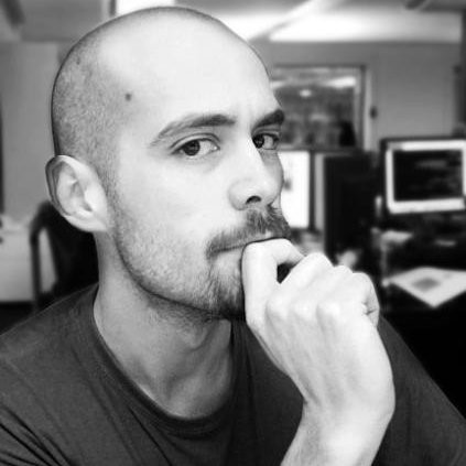 Black and white portrait of a bald man with a mustache and beard, resting his chin on his hand in a thoughtful pose.