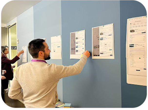 Two people reviewing printed wireframe designs pinned on a blue wall in an office.