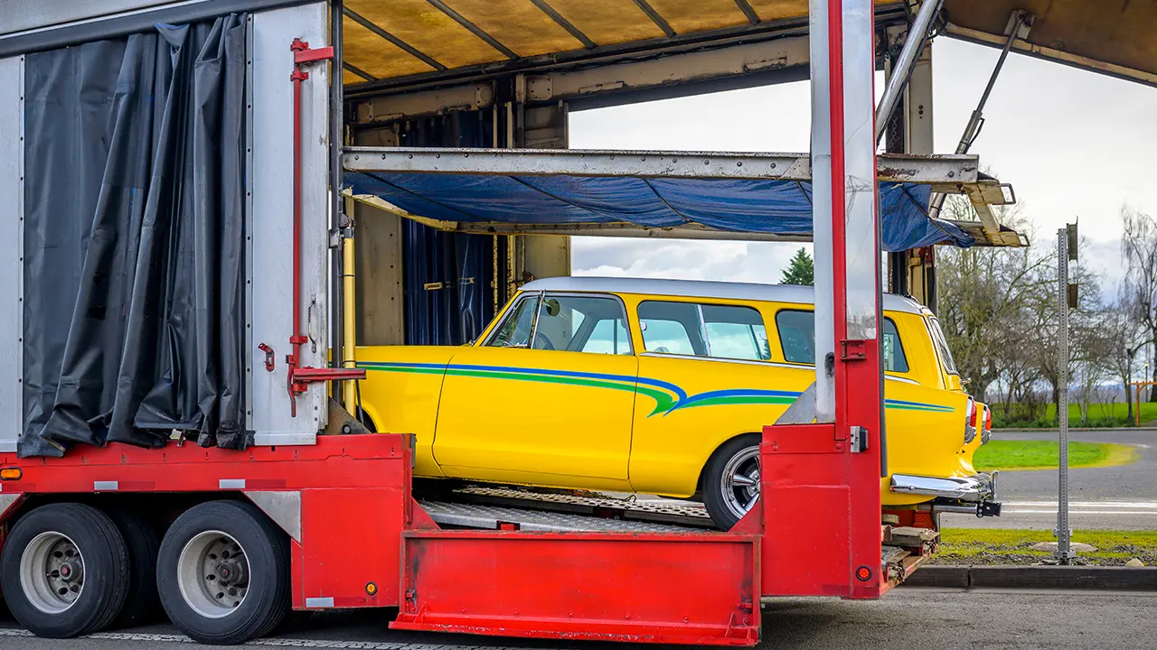 Yellow car loaded on an enclosed car hauling trailer.