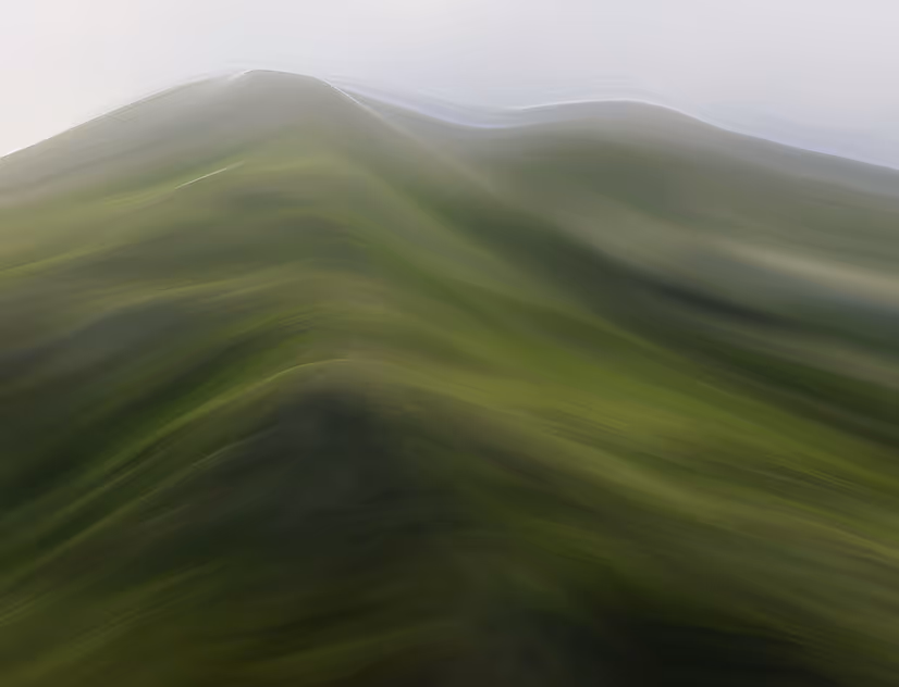 Abstract blurred image of green hills under a pale sky.