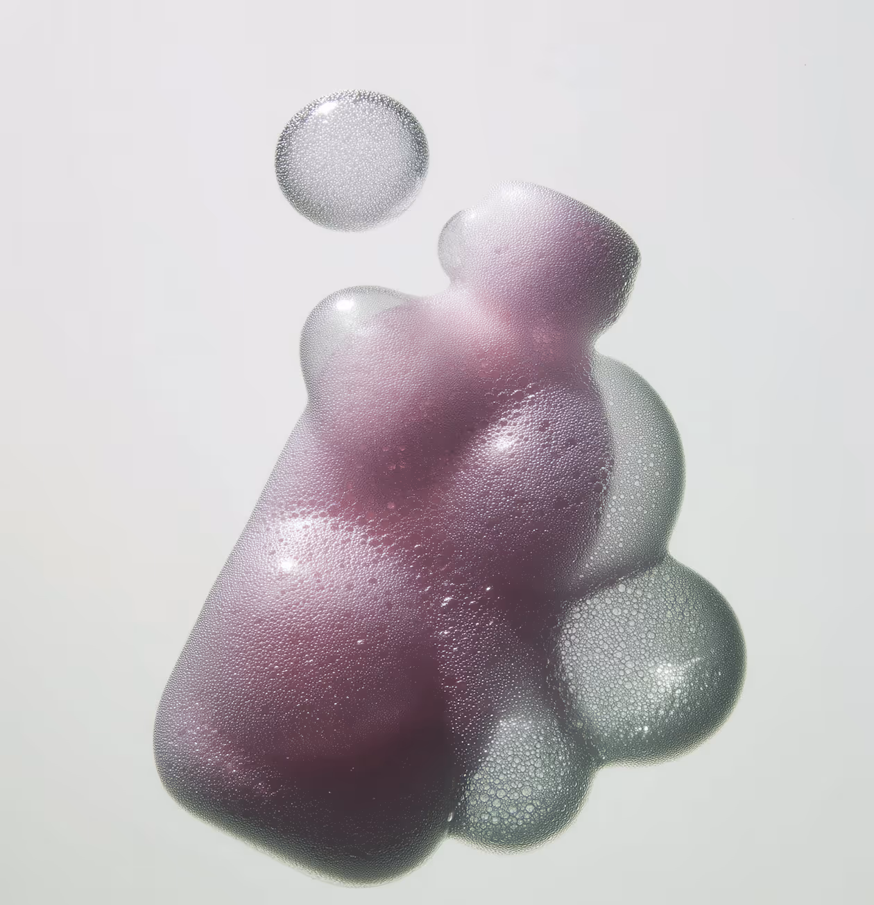 Close-up of a translucent cluster of bubbles with a pinkish tint against a light background.
