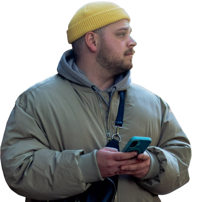 Ein Mann mit gelber Mütze und beige Jacke hält ein Smartphone und schaut nach rechts.