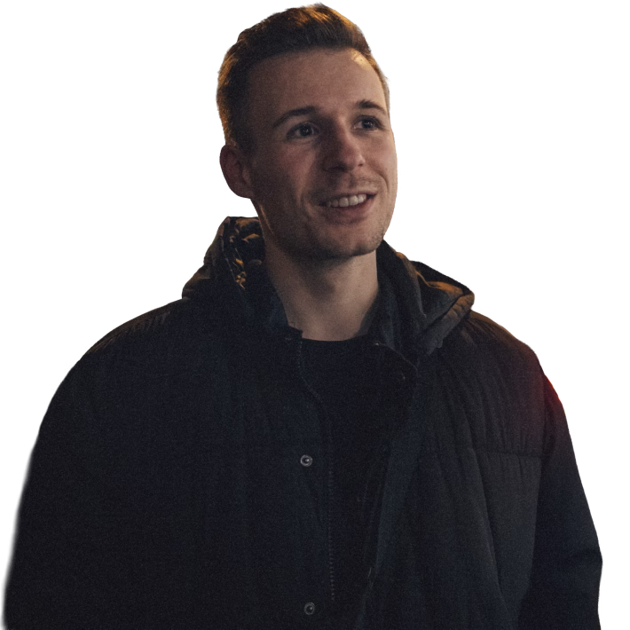 Junger Mann mit dunkler Jacke lächelt und schaut leicht nach oben rechts.