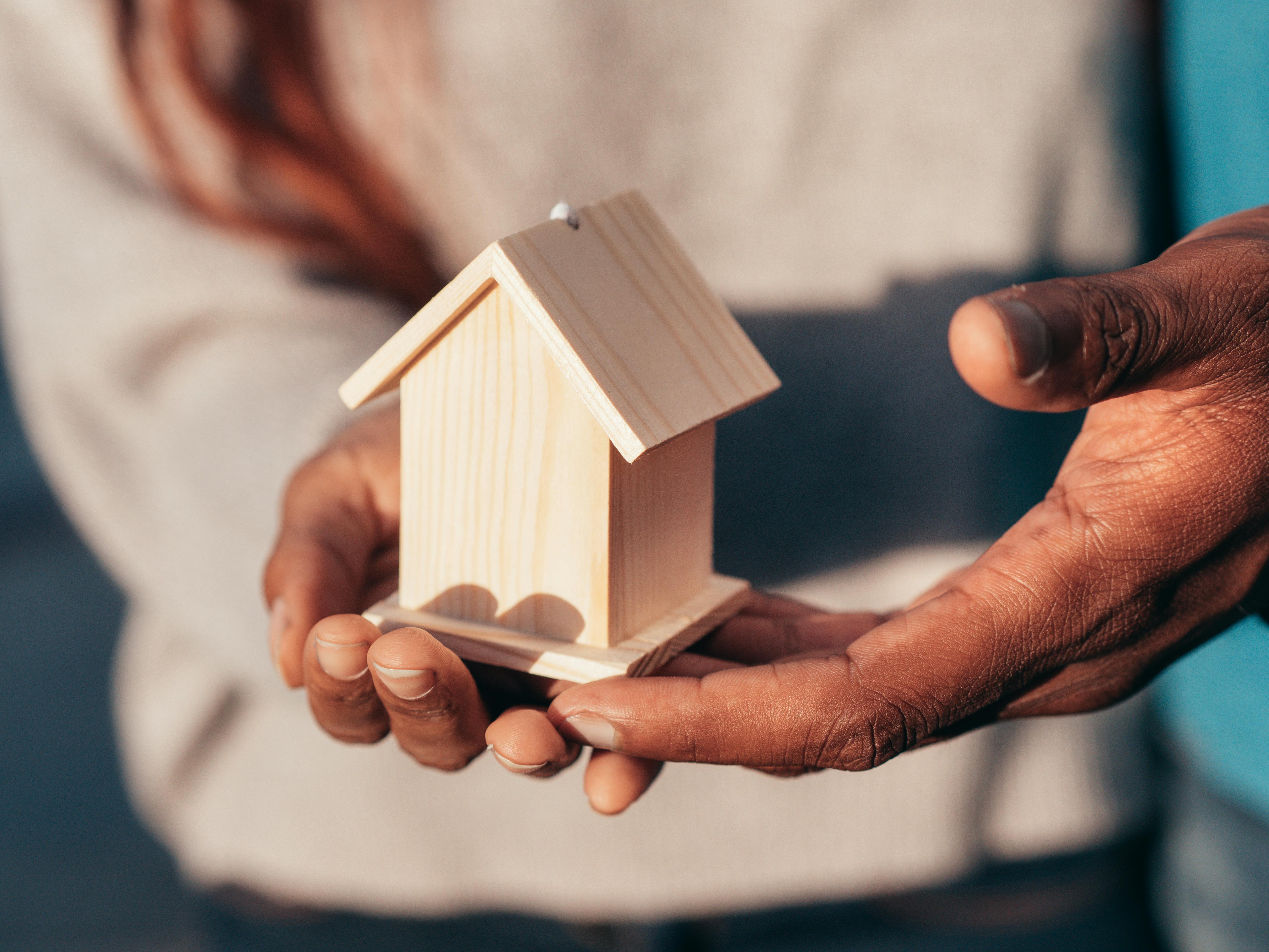 Close-up of hands holding a small wooden house model.