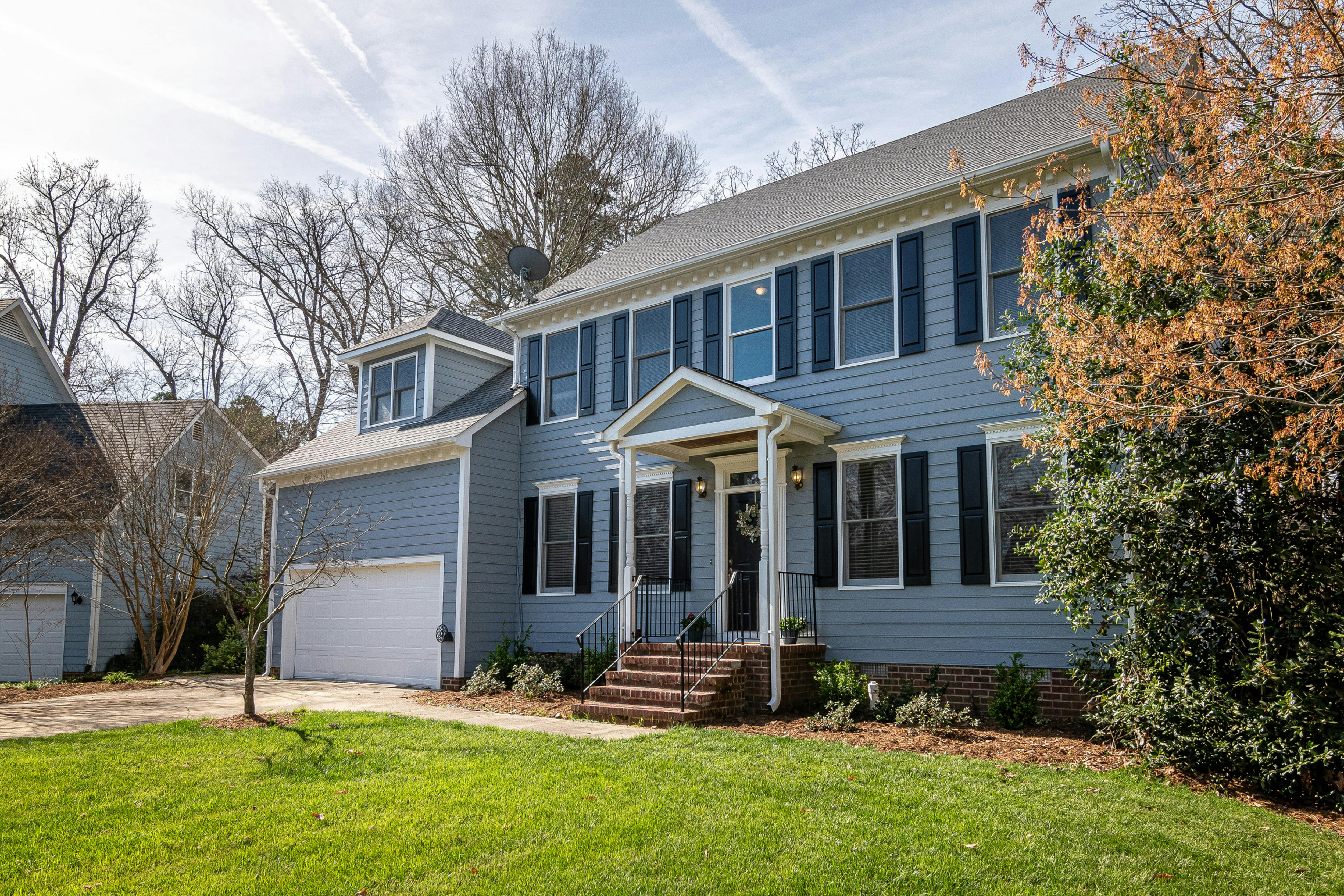 Two-story blue house with black shutters, a white porch with columns, a brick staircase, and a double garage.