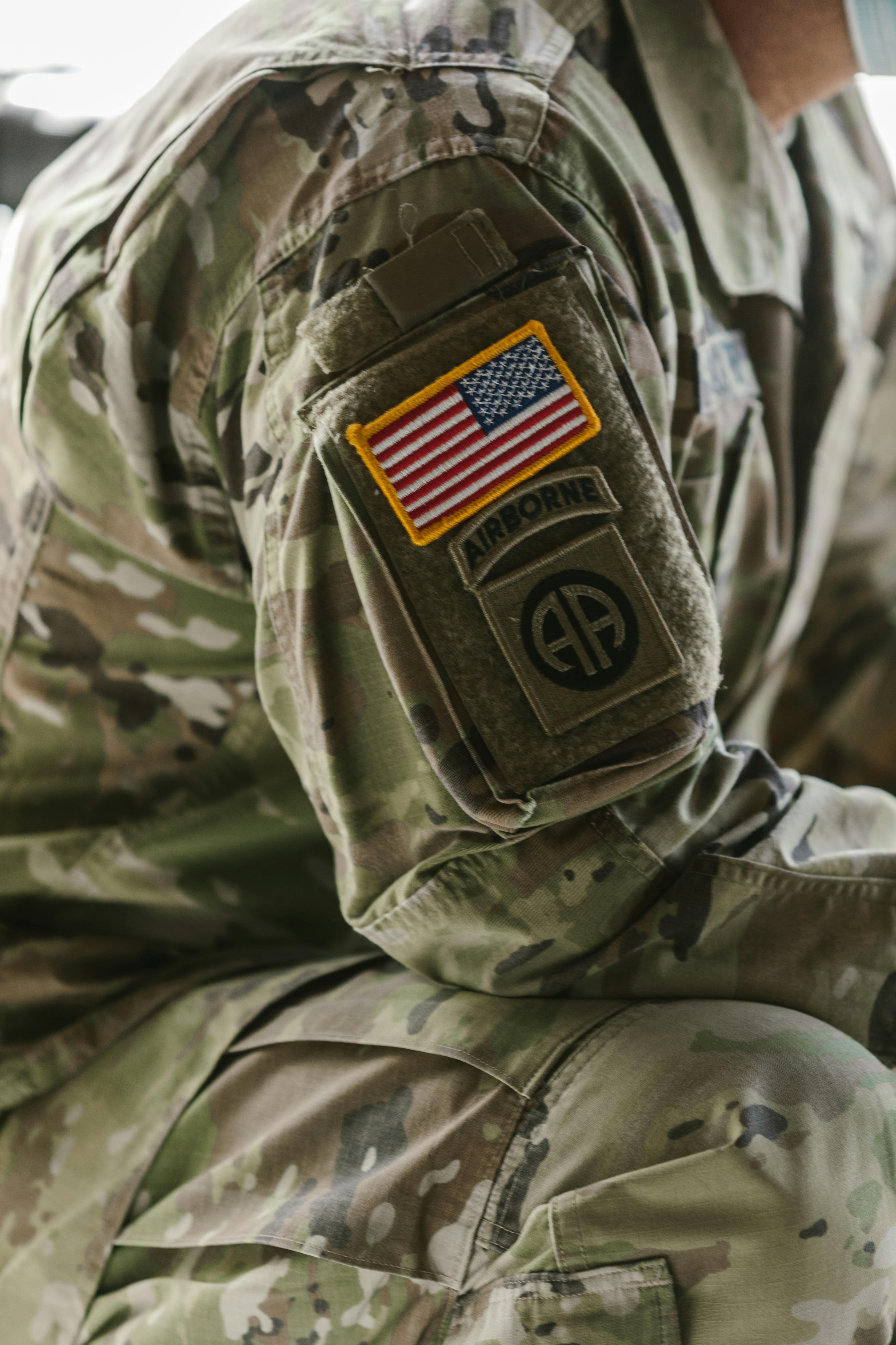 Close-up of a soldier wearing camouflage uniform with an American flag and Airborne patches on the sleeve.