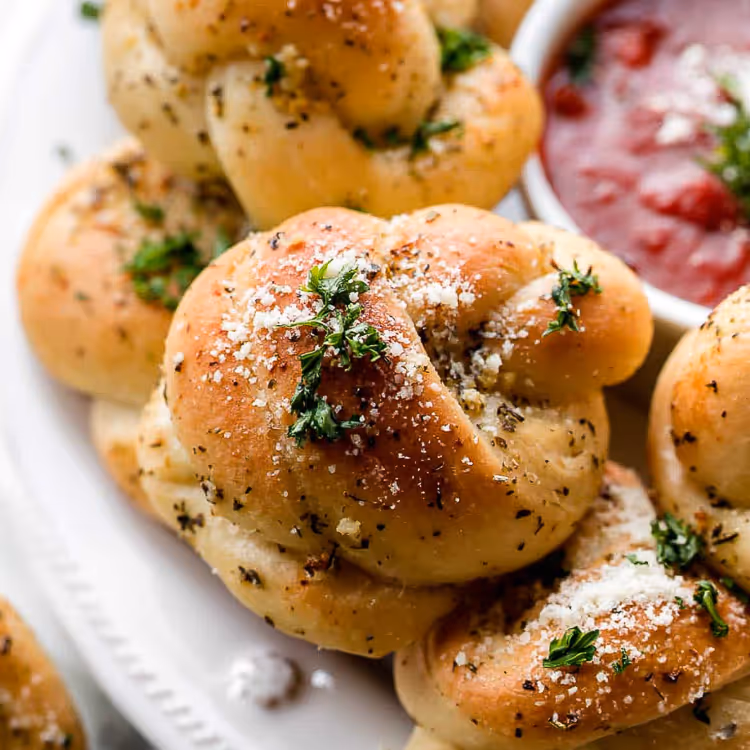 Garlic knots sprinkled with herbs and parmesan, served with a side of marinara sauce.