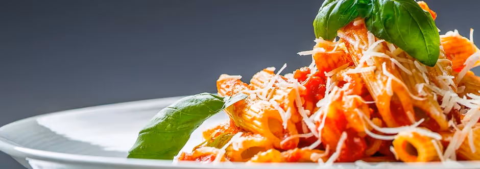 Plate of rigatoni pasta with tomato sauce, grated cheese, and fresh basil leaves.