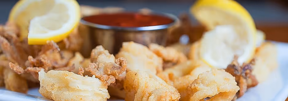 Close-up of crispy fried calamari served with lemon wedges and a small container of marinara sauce.