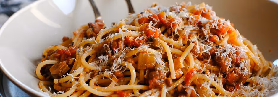Plate of spaghetti with meat sauce topped with grated cheese.