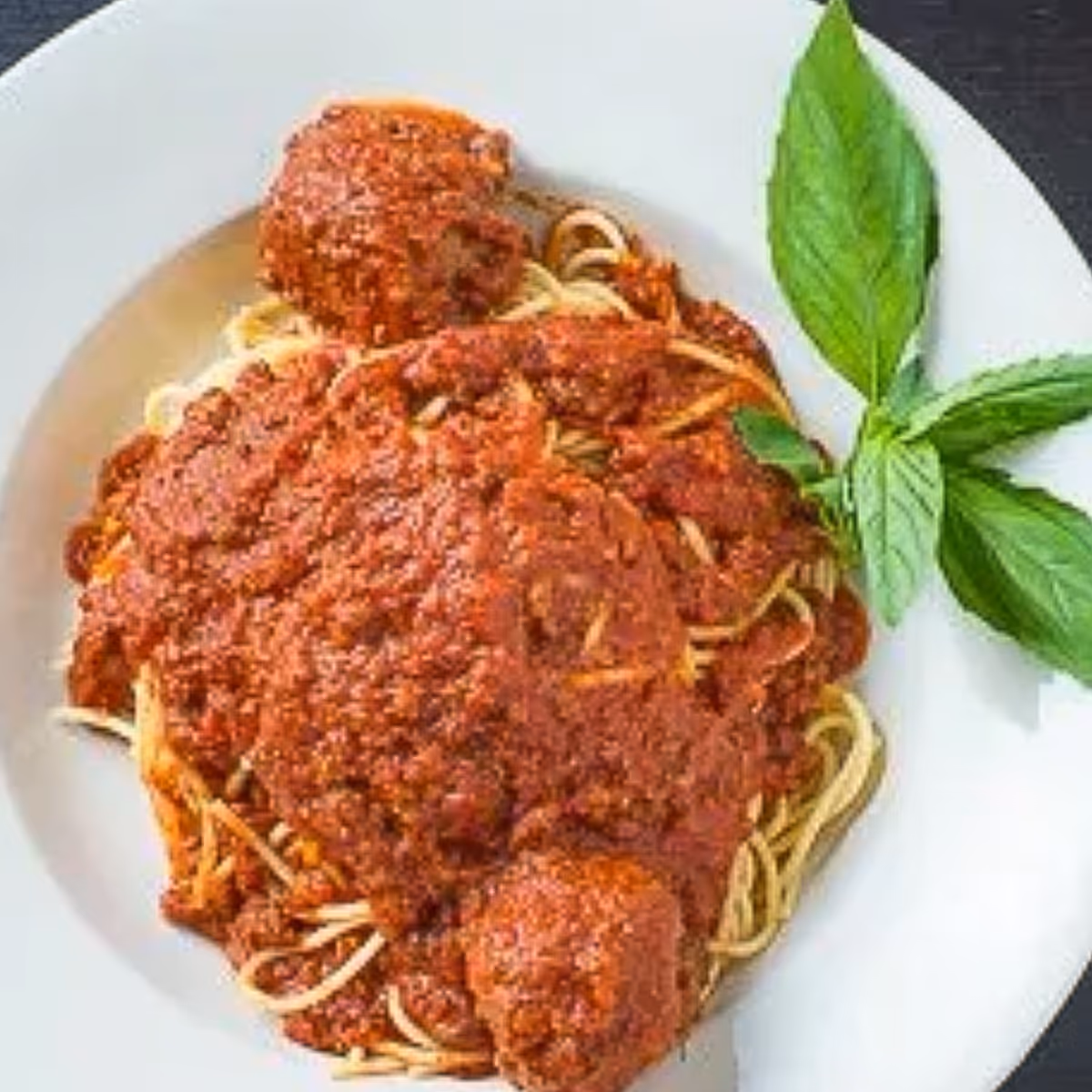 Plate of spaghetti topped with tomato meat sauce and meatballs, garnished with fresh basil leaves.