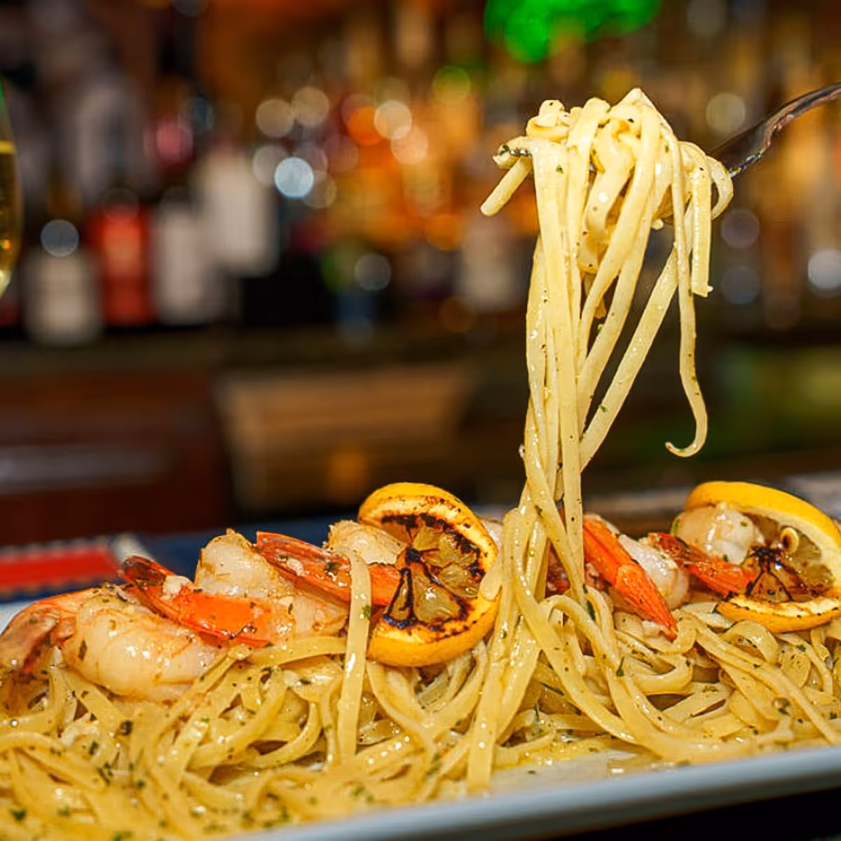 Plate of linguine pasta with shrimp and grilled lemon slices, with pasta lifted on a fork.