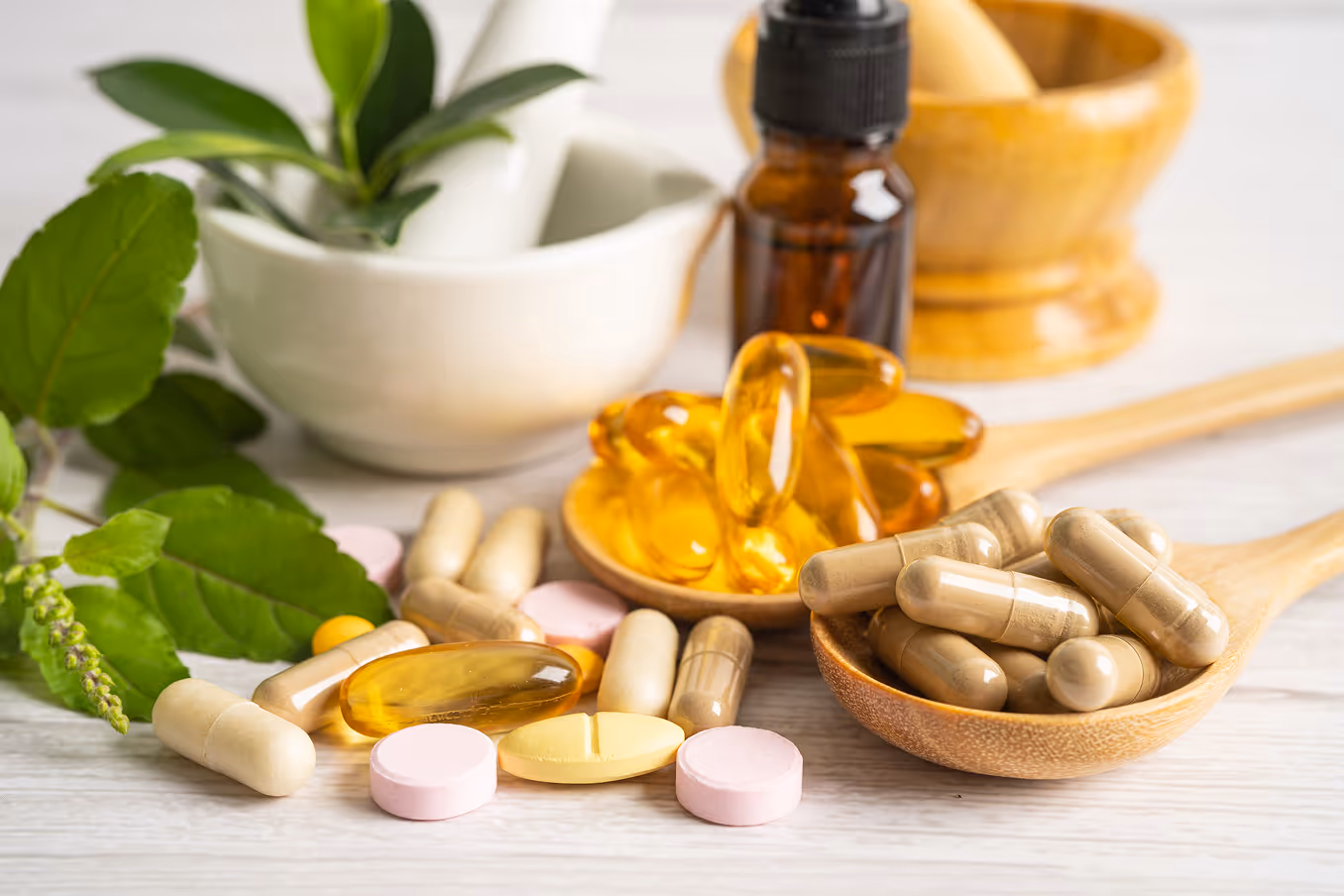Various herbal supplements and capsules with green leaves and a mortar and pestle in the background.