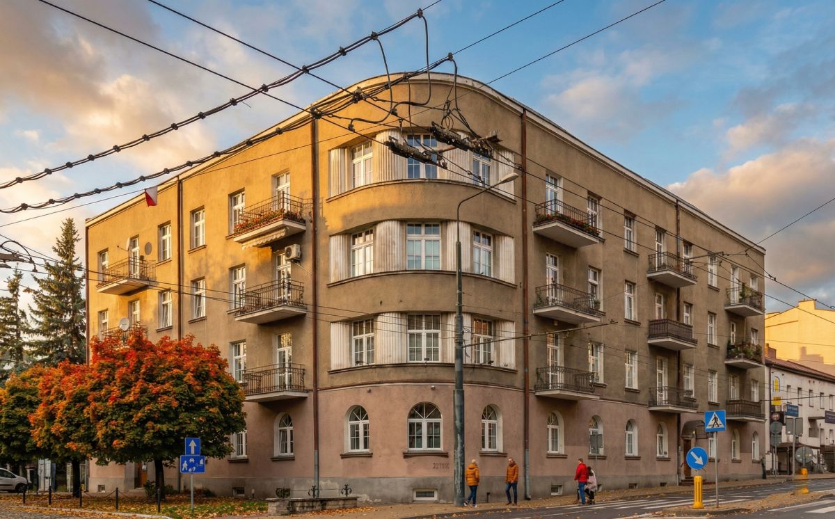 Four-story beige apartment building on a street corner during golden hour with pedestrians walking on the sidewalk.
