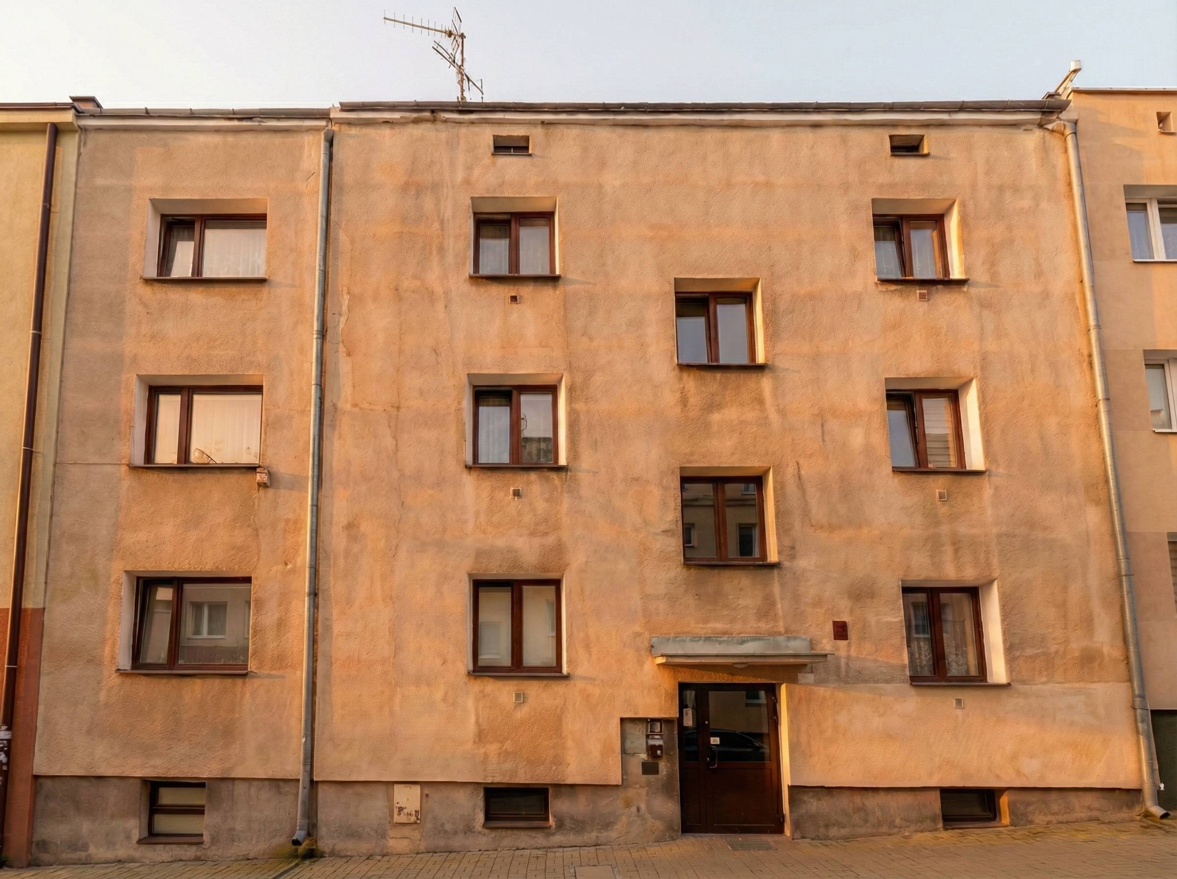 Three-story beige apartment building with multiple windows and a dark brown entrance door.