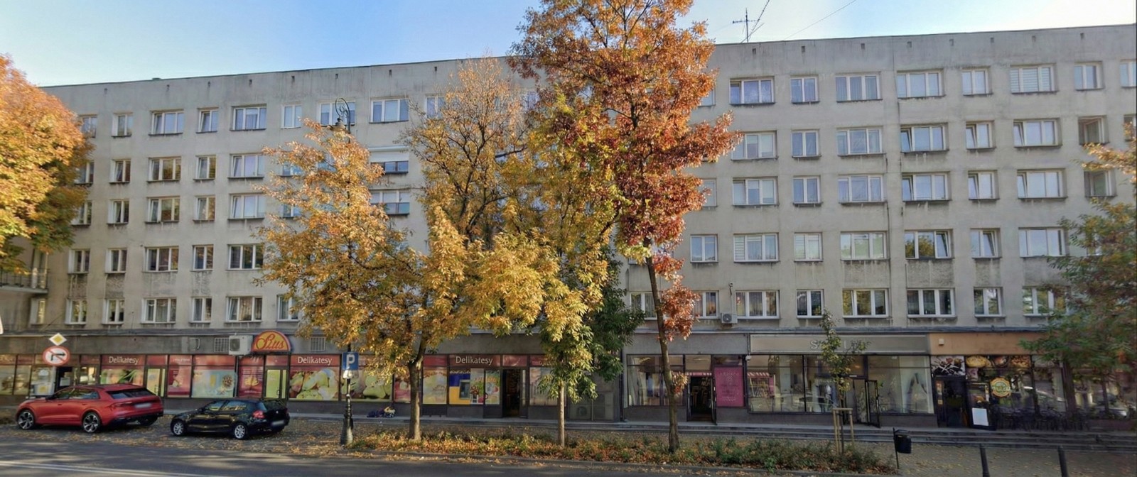 Street view of a six-story residential building with autumn-colored trees and parked cars in front.