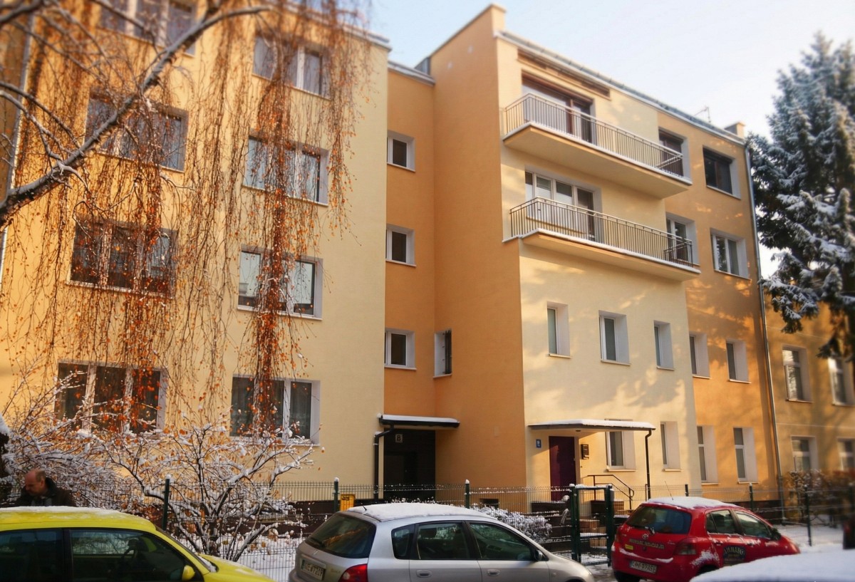 Snow-covered residential building with three parked cars in front on a winter street.