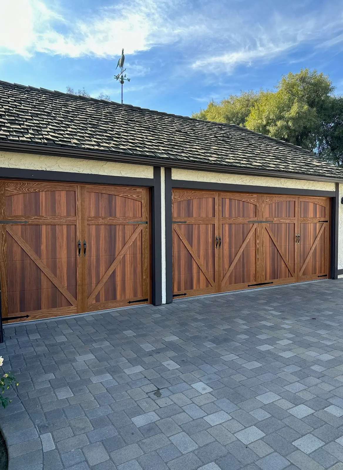 Double garage with two wooden doors featuring a carriage-house design and black handles, gray paved driveway, and a roof with a bird-shaped weathervane.