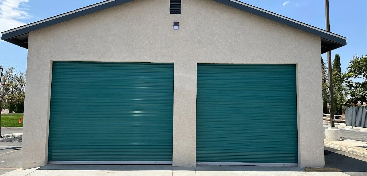 Building with two closed green metal rolling garage doors under a clear blue sky.