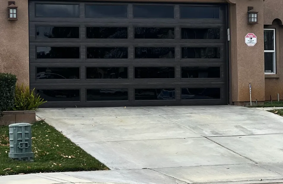 Dark wood and glass-paneled garage door on a stucco house with concrete driveway and small green lawn on the left.