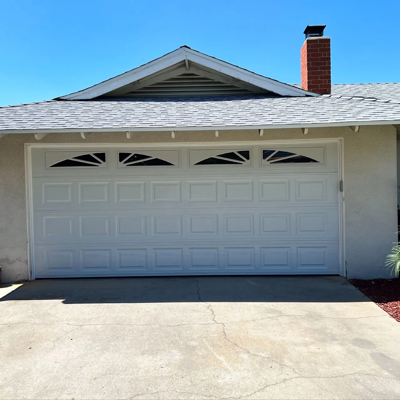 Closed white sectional garage door with four sunburst-style windows at the top under a gable roof with a chimney on the right side.