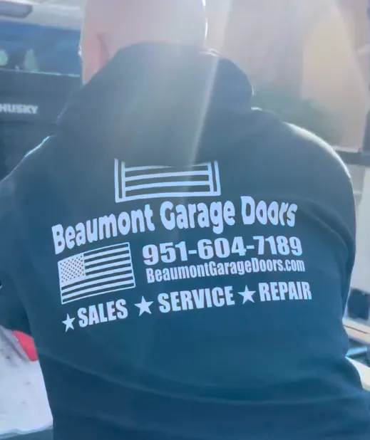 Person wearing a black hoodie with white text advertising Beaumont Garage Doors, including phone number, website, and services: sales, service, and repair, alongside American flag graphics.