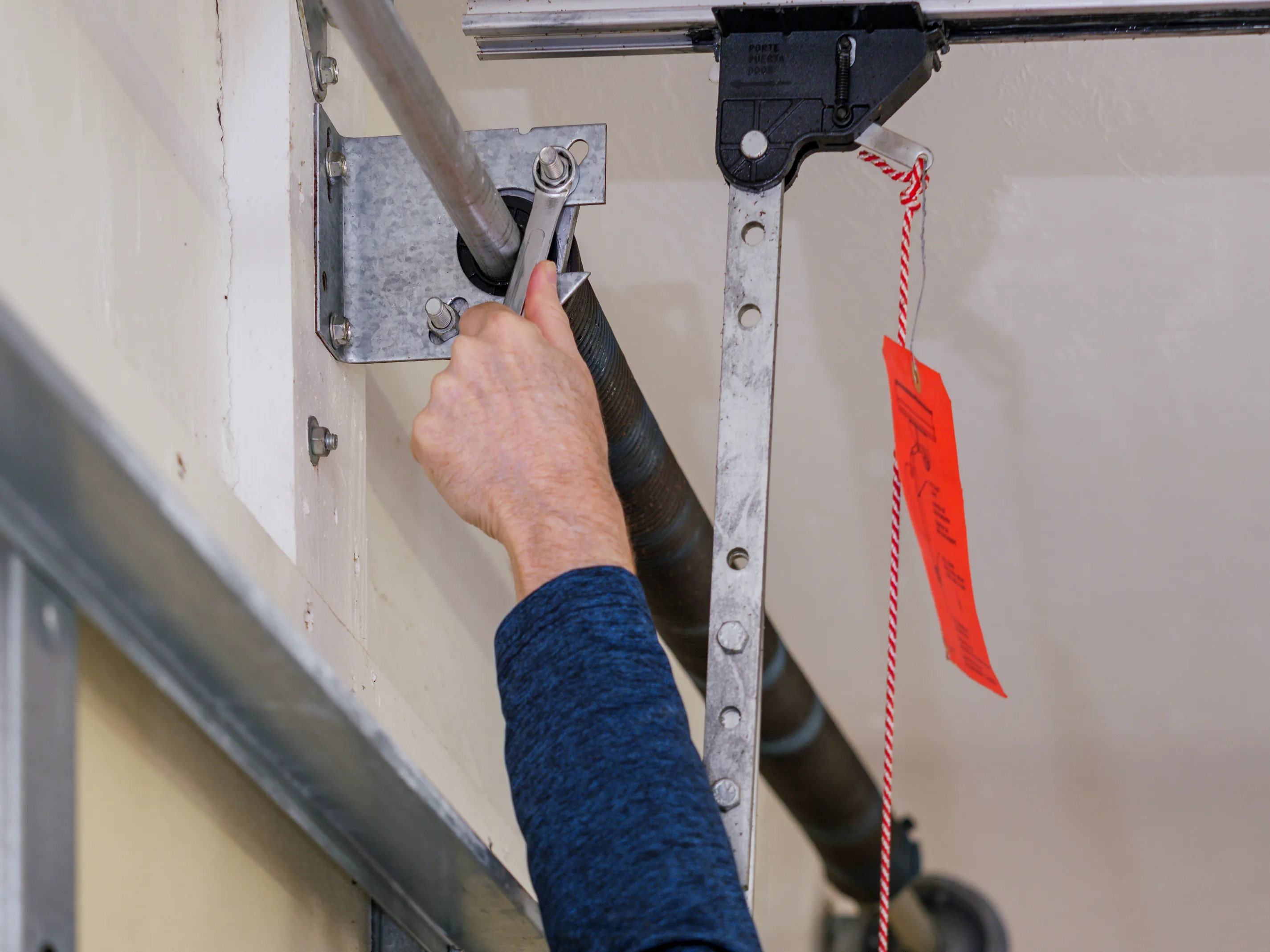 Person using a wrench to adjust a garage door torsion spring system inside a garage.