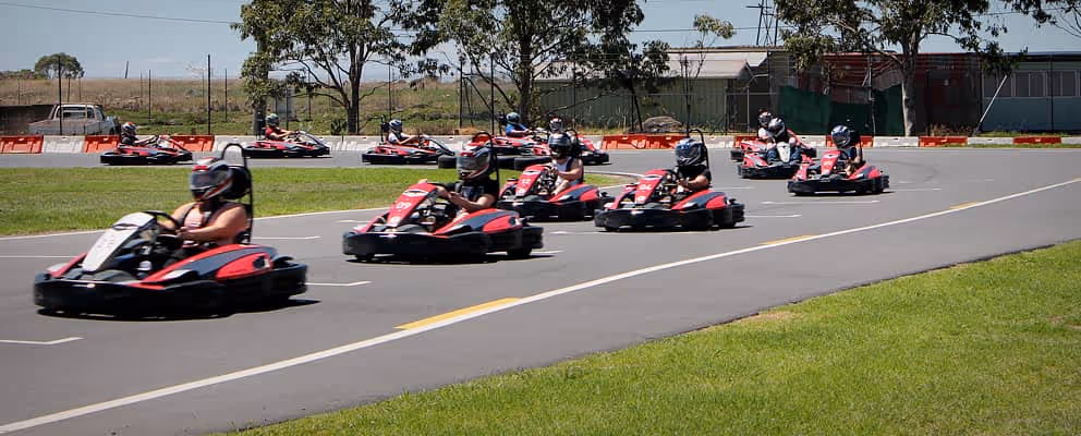 Group of racers driving go-karts around an outdoor track.