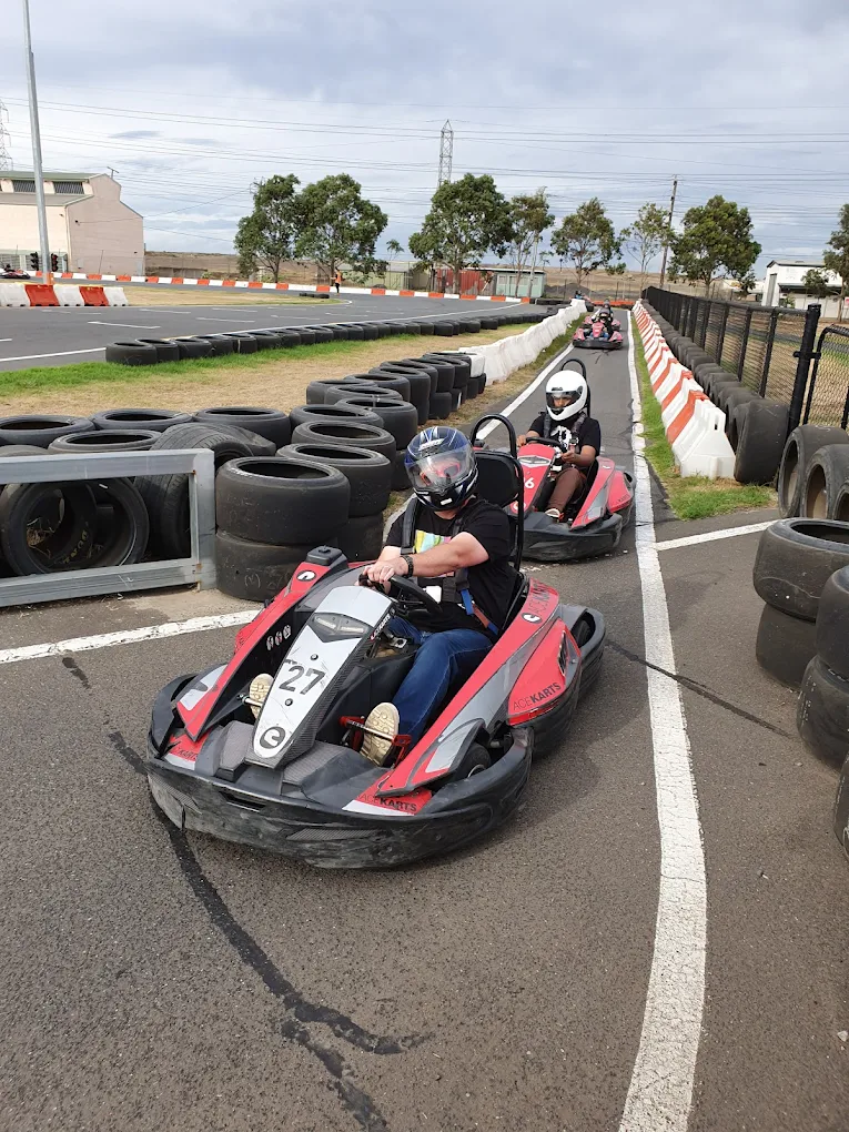 Go-kart racers driving red karts on an outdoor track lined with tyre barriers.