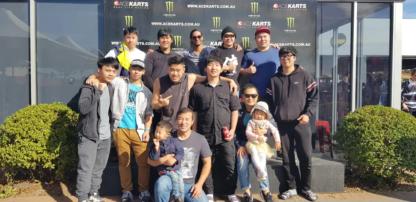 Group posing together at Ace Karts in front of the branded backdrop.