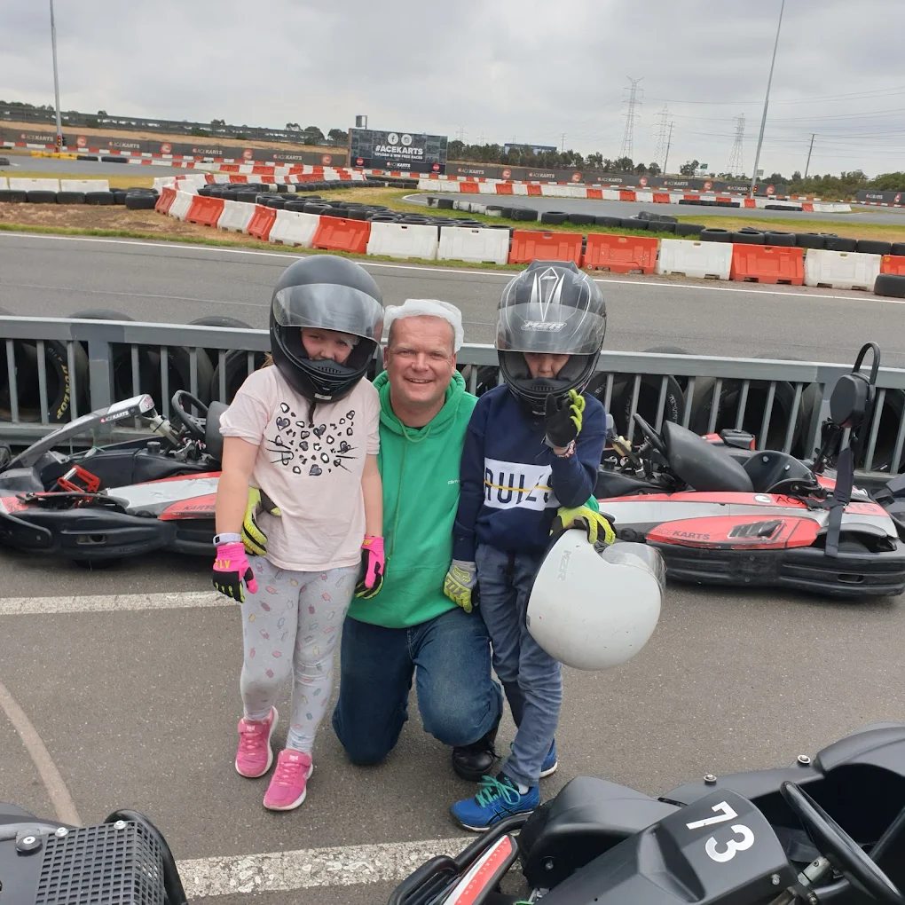 Group posing together in helmets at Ace Karts beside the track and go-karts.