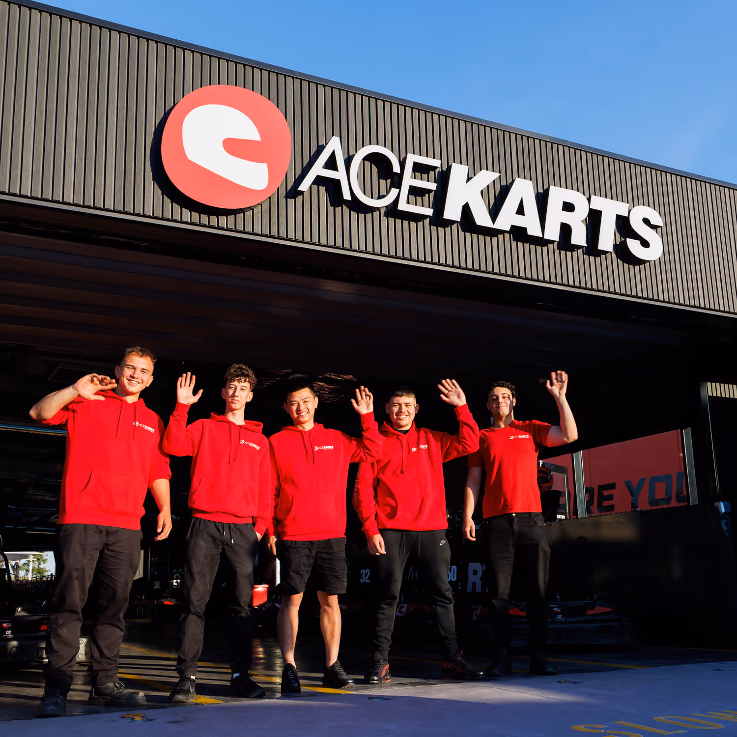 Drivers seated in go-karts inside the Ace Karts pit area while staff in orange vests provide instructions before a race.