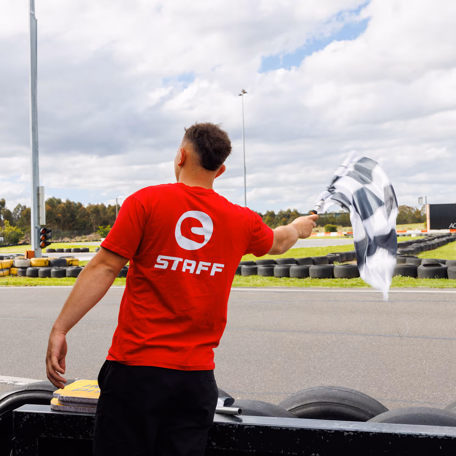 AceKart staff member waving a checkered flag at a go-kart track.