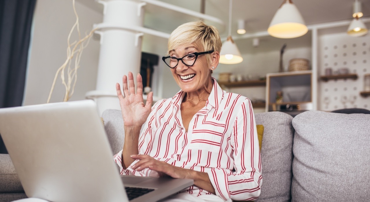 Smiling woman with short blonde hair waving at her laptop during a video call