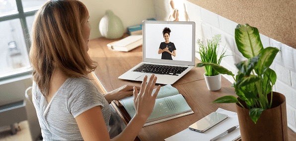 Woman sitting at a desk hand moving up toward a laptop screen displaying a person signing help