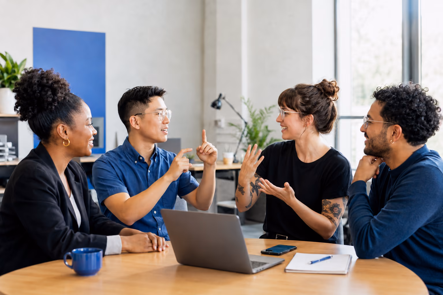 Four professionals using sign language while collaborating around a laptop.