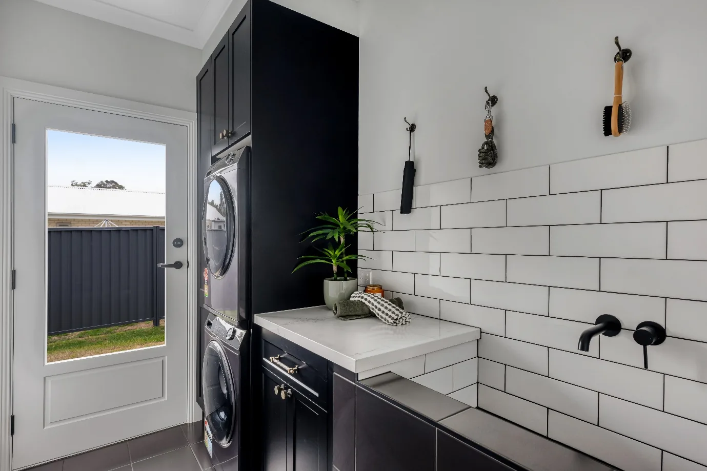 Modern laundry with subway tiles, black cabinetry and wall hooks holding grooming tools near an external door