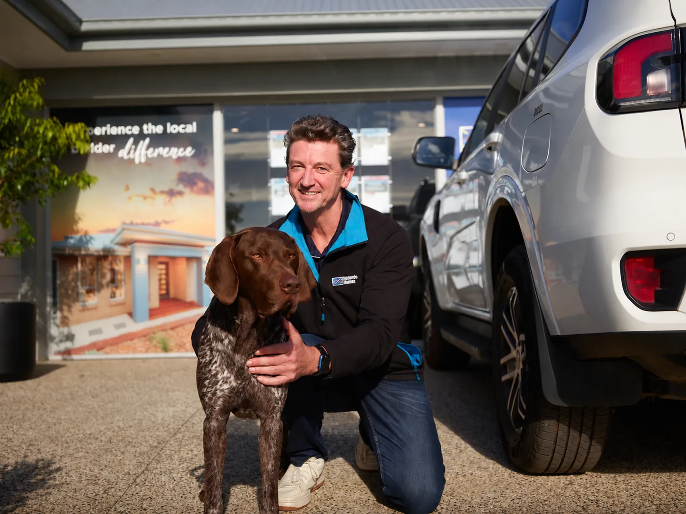 Hotondo Homes builder kneeling beside Hunter, a German Shorthaired Pointer, outside a display home