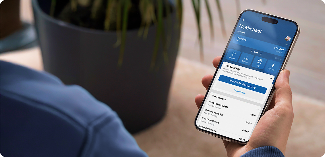 Hand holding smartphone displaying a banking app with account balance, early pay option, and recent transactions.