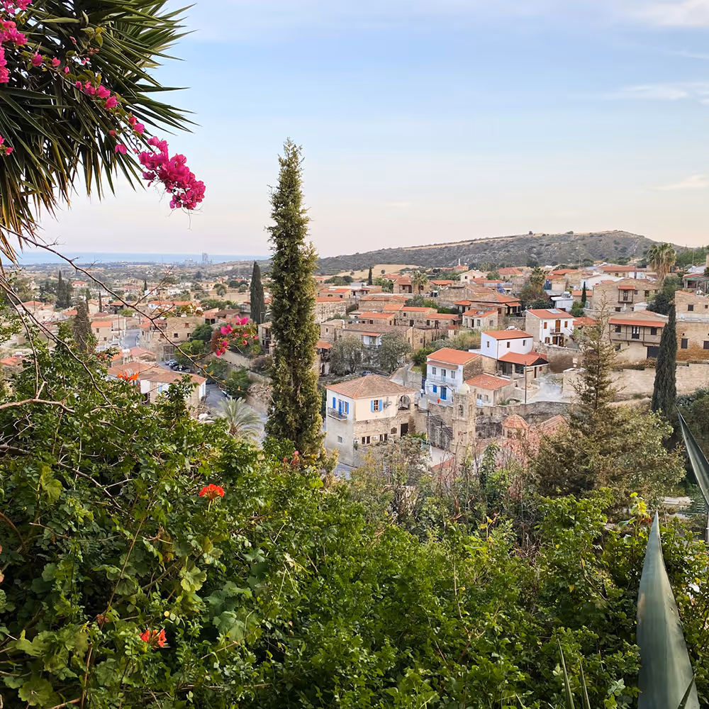 Scenic view of a Mediterranean village with stone houses, terracotta roofs, and lush greenery in the foreground.