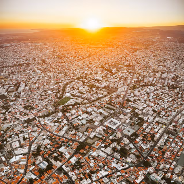 Aerial view of a densely packed urban area with many buildings under a bright orange sunset.